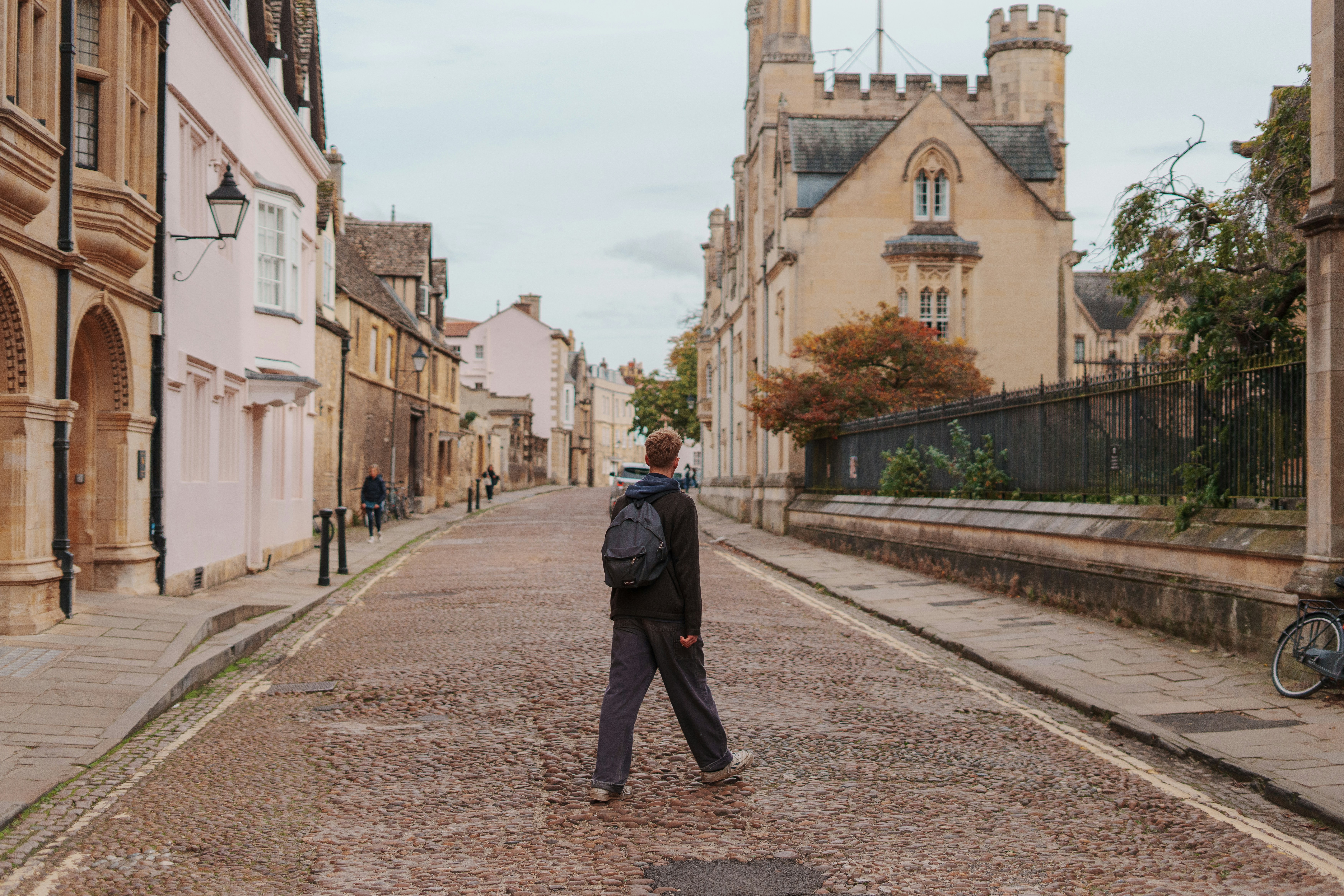 A student walking across a cobbled Oxford street